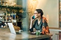 Woman at cafe making a phone call and using laptop computer. Beautiful young woman sitting at coffee shop working on laptop and Royalty Free Stock Photo