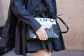 Woman with Cahu black leather bag holding iPhone smartphone in hand before Prada fashion show, Milan Fashion Week