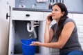 Woman Calling Plumber While Collecting Water Leaking From Sink