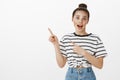 Woman cannot hide her amazement. Fascinated excited young girl with bun hairstyle in striped t-shirt, pointing at upper