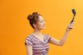 Woman capturing herself with small personal camera on yellow background