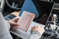 Woman in the car with laptop and passport in a pink cover. Travel concept. Royalty Free Stock Photo