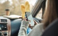 Woman in a car in warm socks is holding a mobile phone gadget. Cozy autumn weekend trip. Freedom of travel Royalty Free Stock Photo