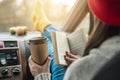 Woman in a car in warm yellow socks is reading a book while sitting in the passenger seat. Cozy autumn weekend trip Royalty Free Stock Photo