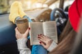 Woman in a car in warm yellow socks is reading a book while sitting in the passenger seat. Cozy autumn weekend trip Royalty Free Stock Photo