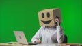 Woman in cardboard box with smiling emoji on her head on studio green background. Employee talking on smart phone Royalty Free Stock Photo