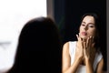 Woman caring of her beautiful skin on the face standing near mirror in the bathroom. Young woman applying moisturizer on her face Royalty Free Stock Photo
