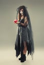 Woman in a carnival costume of a witch or a dead bride holding an apple in her hands, gothic woman in witch costume on gray Royalty Free Stock Photo