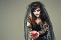 Woman in a carnival costume of a witch or a dead bride holding an apple in her hands, gothic woman in witch costume on gray Royalty Free Stock Photo