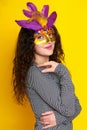 Woman in carnival mask with feather, beautiful girl portrait on yellow color background, long curly hair Royalty Free Stock Photo