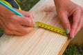 Woman carpenter doing a tape measure on a wooden board on the lawn near the house. Close-up view of hands with a measuring tool Royalty Free Stock Photo