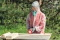 Woman carpenter in respirator, goggles and overalls handles a wooden board with a Angle grinder Royalty Free Stock Photo