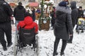 A woman carries a man in a red jacket with a disability in a wheelchair