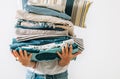 Woman carrying the big pile blue and beige laundry in her hands. Woman`s Home work concept image