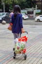 Woman carrying groceries in shopping cart full of throw-away plastic shopping bags