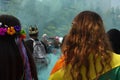 Woman carrying rainbow flag on her back next to woman with all rainbow flowers amid blue green haze and crowds of people at the LG