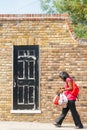 Woman carrying shopping bags in red top walks past brik wall with peeling black painted door