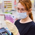 Woman cashier in a medical mask counts money against the background of the cash register. Euros in the hands of the seller in the Royalty Free Stock Photo