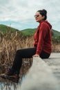 Woman with casual clothes and sunglasses sitting on a wooden walkway and surrounded by cane and rushes on a lake Royalty Free Stock Photo