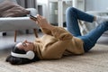 Woman in casual clothing with headphones lying down the floor in her living room and listening the music from her phone Royalty Free Stock Photo