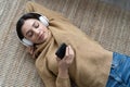 Woman in casual clothing with headphones lying down the floor in her living room and listening the music from her phone Royalty Free Stock Photo