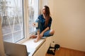 Woman in casual denim clothes sitting on the window sill and drinking coffee Royalty Free Stock Photo