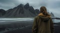 Woman in light jacket standing on black sand beach Iceland volcanic mountains Royalty Free Stock Photo