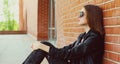 Woman in casual sitting in the city wearing a black rock style over a brick wall background Royalty Free Stock Photo