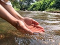 Woman catches running water in her cupped hands at waterfall.