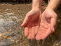 Woman catches running water in her cupped hands at waterfall.