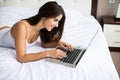 Woman catching up on her social media as she relaxes in bed with a laptop computer on a lazy day Royalty Free Stock Photo