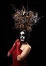 Woman of Caucasian appearance with skeleton make-up stands in a red velor dress with a large crown of dry branches