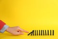 Woman causing chain reaction by pushing domino tile on yellow background, closeup. Space for text Royalty Free Stock Photo