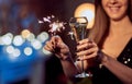 Celebrating New Years Eve, happy woman toasting with champagne, holding sparkler or bengal light