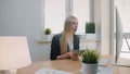 Woman celebrating success in office. Elegant blond female sitting at workplace holding in hands bundle of cash looking Royalty Free Stock Photo