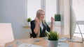 Woman celebrating success in office. Elegant blond female sitting at workplace holding in hands bundle of cash looking Royalty Free Stock Photo