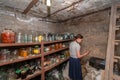 The woman in the cellar is gray-haired, the girl prepares food for the winter, canned food in glass jars on the rack