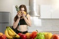 Woman with centimeter round neck wearing black top and leggings bites pineapple and orange in kitchen full of fruits dietology and