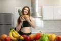 Woman with centimeter round neck wearing black top and leggings hugs pineapple and orange in kitchen full of fruits dietology and