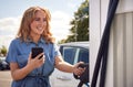 Woman Charging Electric Car With Cable Using App On Phone To Monitor Battery Level Royalty Free Stock Photo