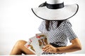 Woman in a check print dress and a big hat holding giant playing cards