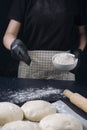 Woman in checkered apron and black gloves sprinkles with flour a table before preparation a piece of yeast dough. Process of Royalty Free Stock Photo