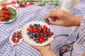 Woman in checkered stylish dress take berry from berries plate. Outdoor picnic