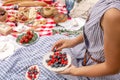 Woman in checkered stylish dress take berry from berries plate. Outdoor picnic