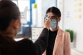 Woman checking colleague temperature using digital thermometer