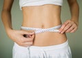 A woman checking her weight loss progress with a measuring tape around her waist. Fitness goals