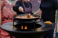 Woman chef cooking paella - fried chicken meat pieces, peppers, peas in huge wok