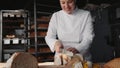 Woman chef cutting healthy bread on wooden board at bakehouse kitchen