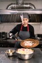 Woman chef in special clothes and rubber gloves, pouring sliced crab sticks into a bowl. Diet salad preparation concept.