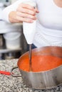 Woman chef whisking boiled tomato sauce in a pot